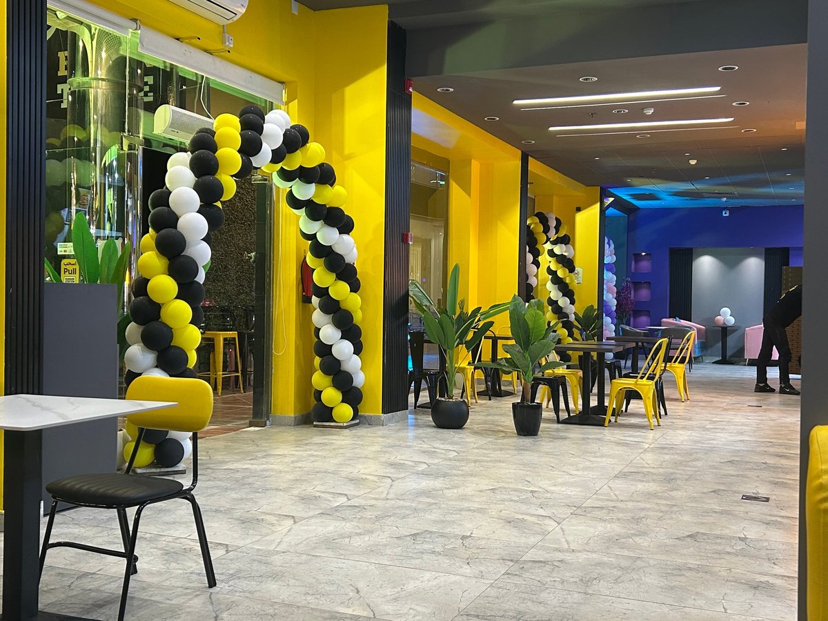Modern event space with yellow and black balloon decorations, bright yellow walls, marble flooring, and contemporary furniture